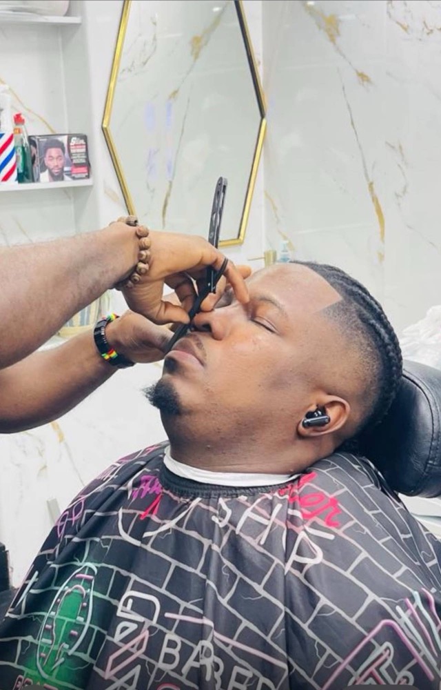 A barber using a straight razor to detail a customer's line-up.